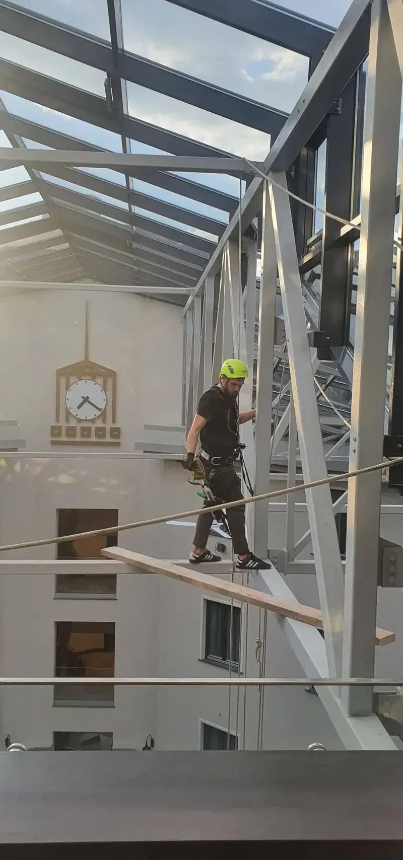 Aukštalipis šalme ir saugos diržais eina stiklinio stogo plieniniu karkasu pastato viduje